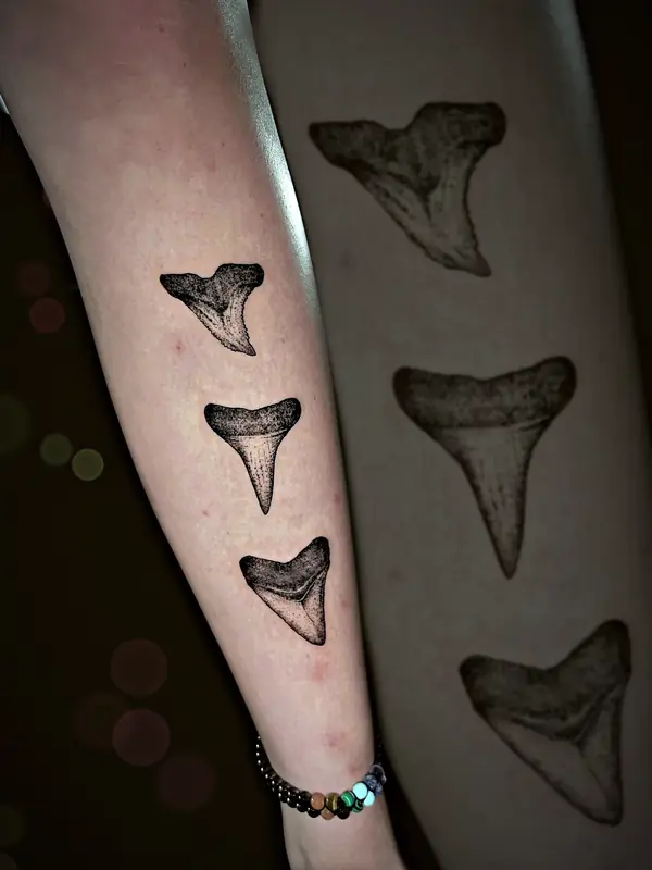 Three shark teeth tattoo by Damián Calandra